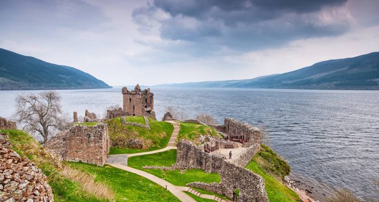 Ruins by the shore of Loch Ness under a cloudy sky.