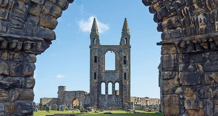 Ruinas de una catedral histórica vistas a través de un arco de piedra irregular que enmarca un cielo brillante.