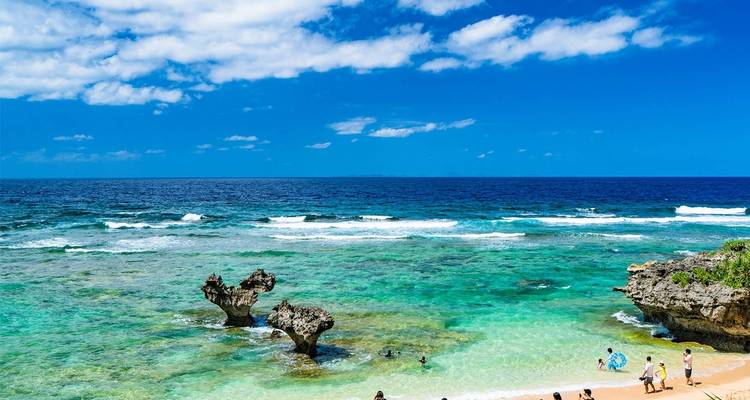 Strand mit Felsformationen und Menschen, die das Wasser genießen.
