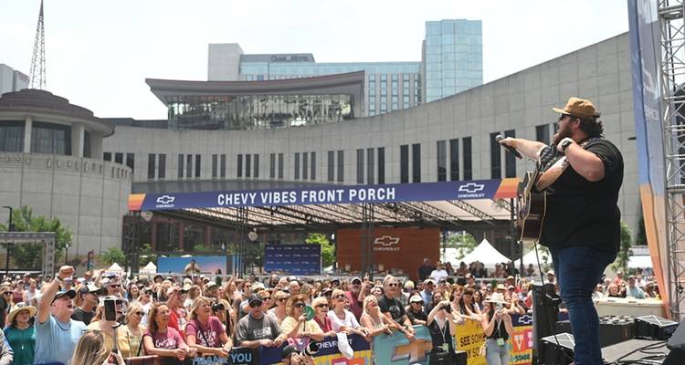 Un musicien se produisant à l'extérieur avec un paysage urbain et une foule en arrière-plan.