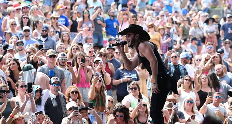 Un chanteur se produisant à l'extérieur avec un large public visible en arrière-plan.