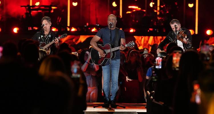 Un groupe qui se produit sur une scène vivement éclairée avec un public devant.