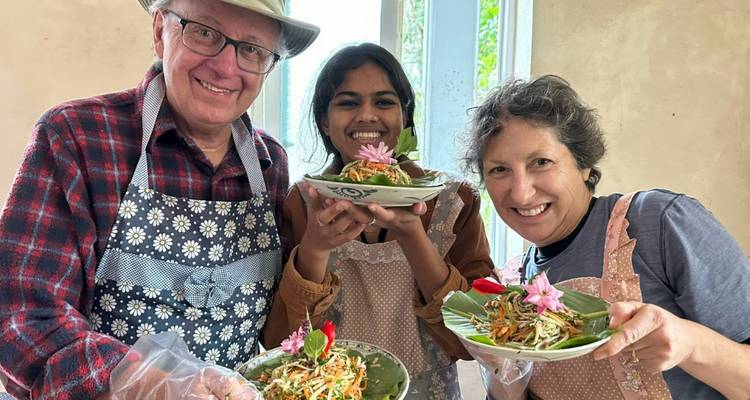 Smiling cooking-class participants present Vietnamese salads garnished with flowers inside rustic kitchen.