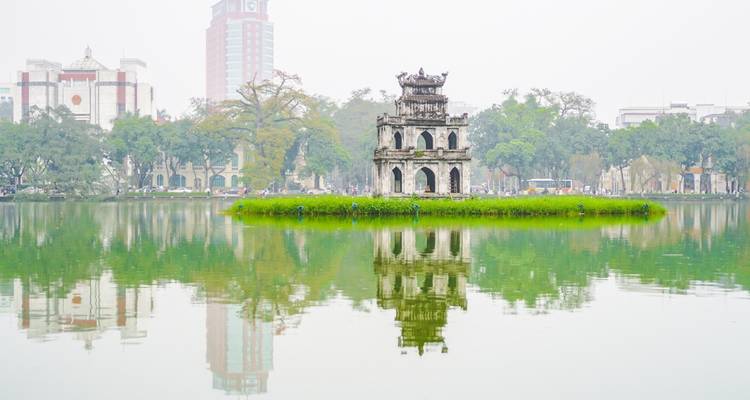 Iconische toren in Hanoi omringd door water met moderne gebouwen op de achtergrond.