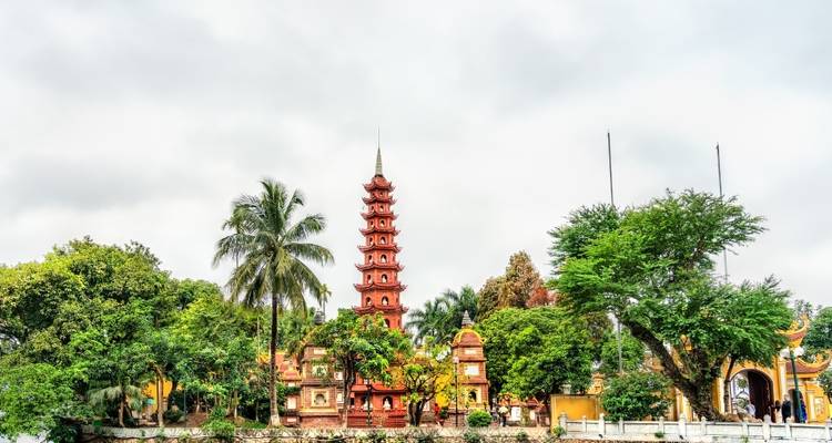 De Tran Quoc Pagoda verheft zich naast een rustig merengebied omzoomd met palmen en bomen.