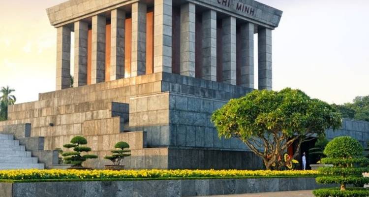 Granieten Ho Chi Minh-Mausoleum omlijst door verzorgde bonsai en goudgeel licht.