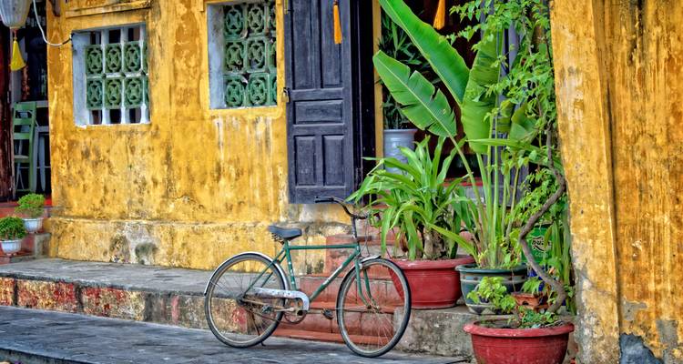 Vintage fiets naast een geel gebouw met potplanten.