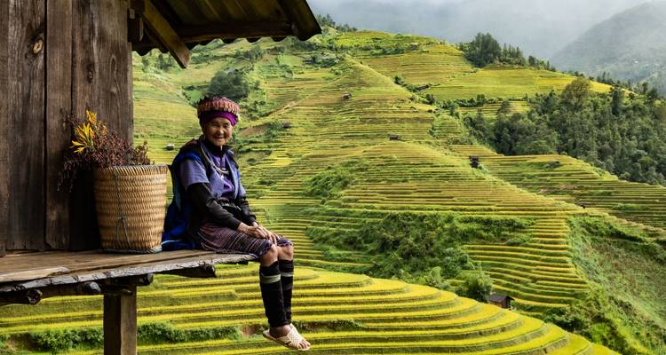 Persoon in traditionele kleding zittend op een huis met uitzicht op rijstterrassen.