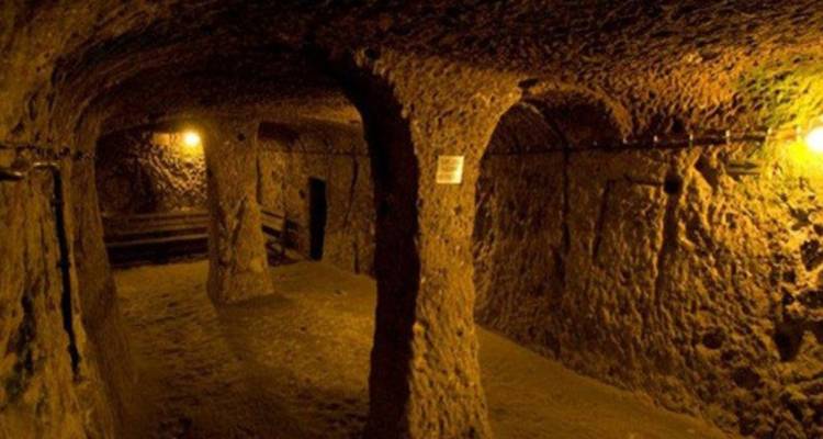 Chambre souterraine avec des colonnes en pierre brute éclairées par des ampoules jaunes à l'intérieur d'un réseau de tunnels historiques.