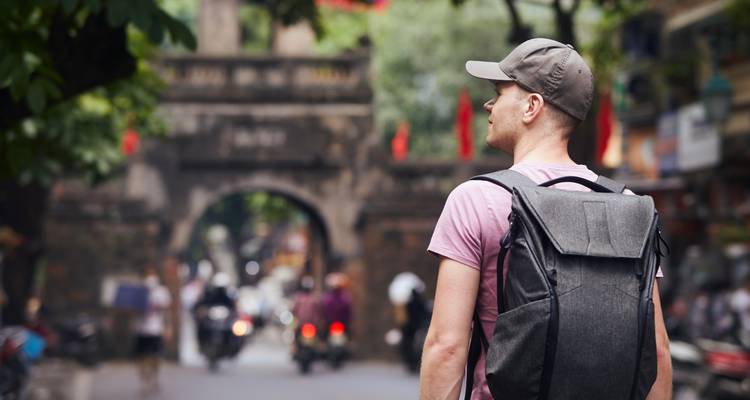 Een man met een rugzak die naar een historische poort kijkt in een drukke straat.