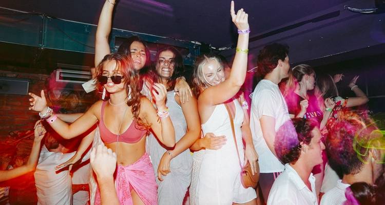 Group of people dancing in a nightclub with colorful lighting.
