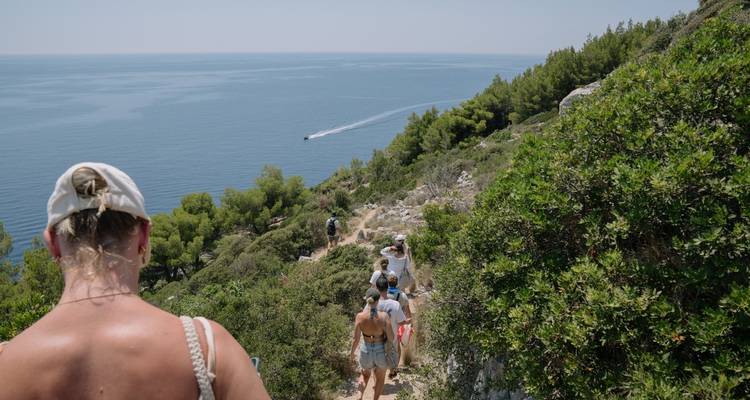 People hiking on a cliffside trail overlooking the sea.