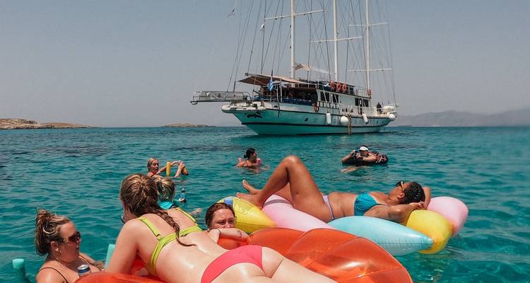 People relaxing on inflatables in the sea with a yacht nearby.