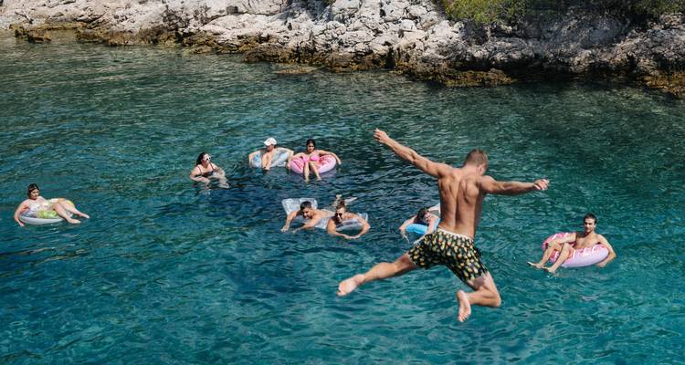 People swimming and jumping into the sea near rocky cliffs.