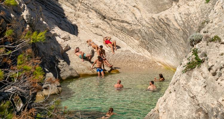 People relaxing near a rocky pool with clear water.