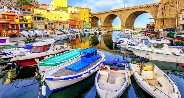 Bateaux de pêche colorés amarrés dans le pittoresque port du Vallon des Auffes sous un viaduc ferroviaire en pierre à Marseille.