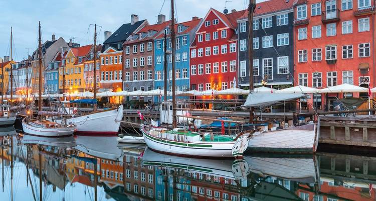 Ikonischer Nyhavn-Kanal mit bunten Stadthäusern, historischen Booten und glasklaren Wasserspiegelungen in der Abenddämmerung.