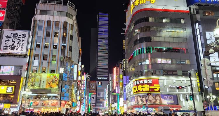 Eine belebte Stadtstraße bei Nacht, voller Menschen und leuchtender Reklametafeln.
