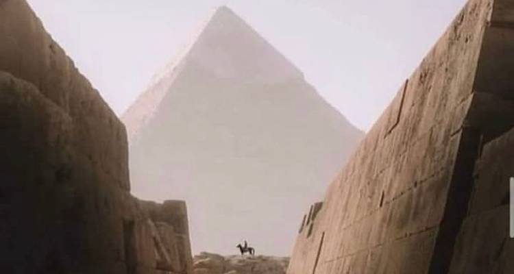 Vue d'une pyramide encadrée par deux grands murs de pierre.