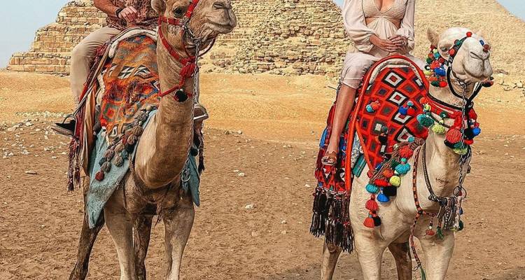 Des gens à dos de chameaux devant des pyramides.