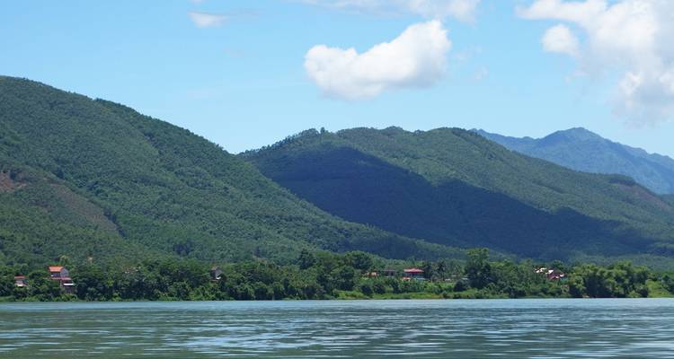 Une large rivière avec des collines boisées sous un ciel bleu.
