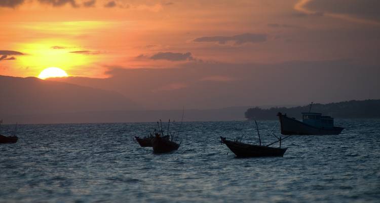 Zonsondergangsuitzicht over de zee met boten die zich afsilhouetteren tegen de horizon.