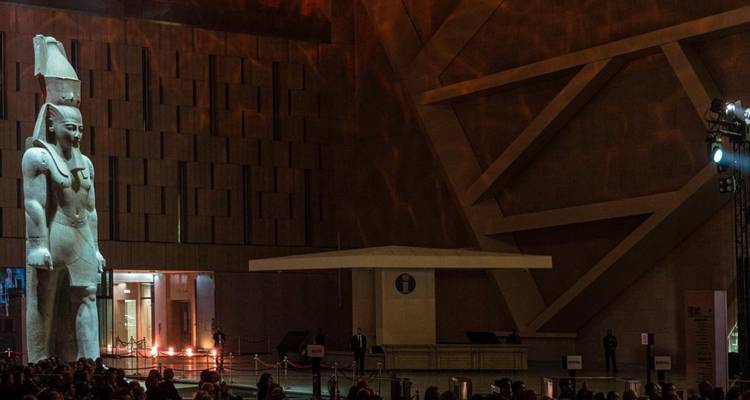 Groot Egyptisch standbeeld in een moderne museumzaal met publiek.