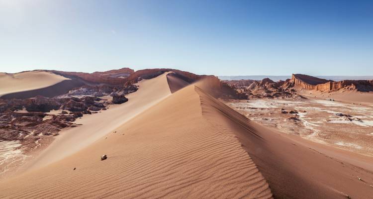 Dune de sable avec des formations rocheuses uniques et un ciel bleu.