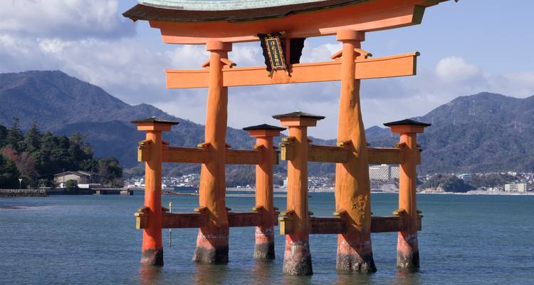 Das berühmte schwimmende Torii-Tor des Itsukushima-Schreins, das im Wasser steht, mit Bergen im Hintergrund.