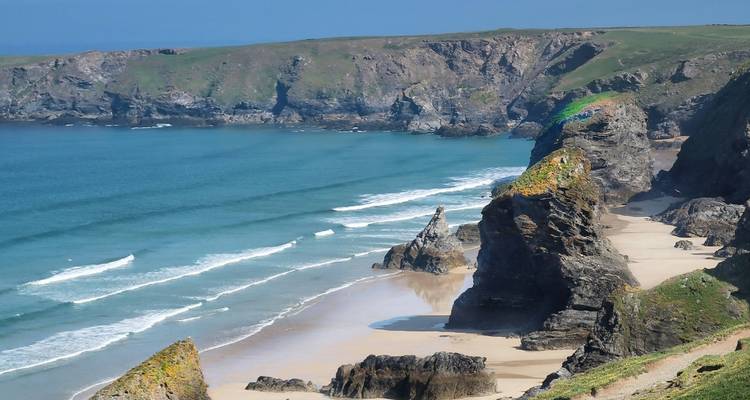Côte rocheuse avec des vagues qui se brisent sur une plage de sable.