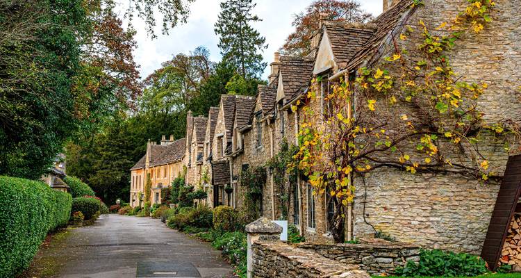 Quaint stone cottages with climbing ivy line a quiet lane in the Cotswolds during autumn.