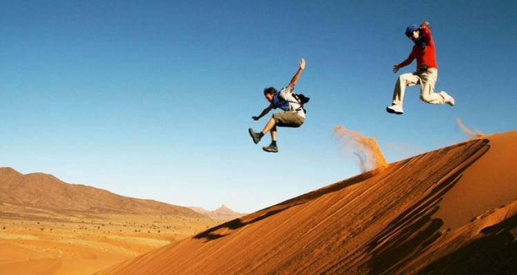 People jumping on desert dunes.