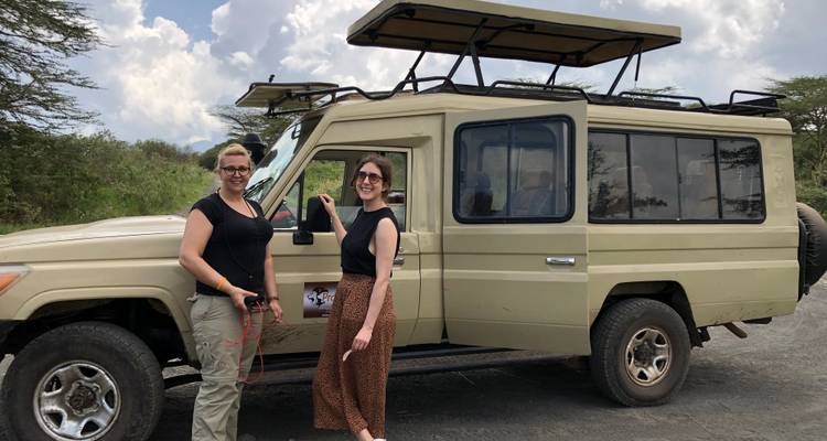 Two women standing beside a safari vehicle.