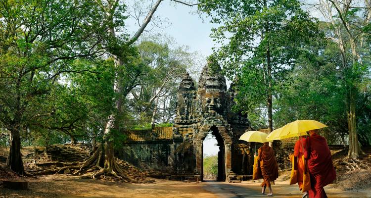 Tres monjes caminando bajo paraguas frente a una puerta antigua.