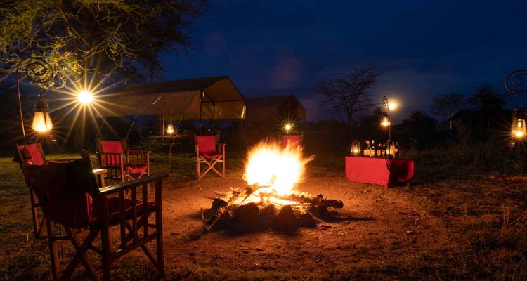 Un camp de safari nocturne avec un feu de camp et des lanternes.