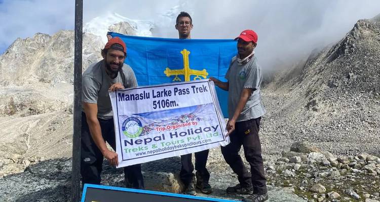 Trois hommes tenant un drapeau devant un panneau de randonnée en montagne.