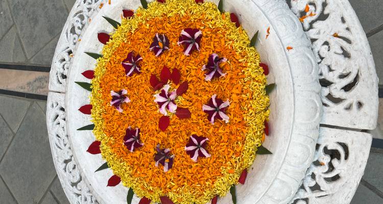 Nahaufnahme einer farbenfrohen floralen Rangoli-Anordnung aus Ringelblumen- und Rosenblättern auf einem geschnitzten Marmortisch.