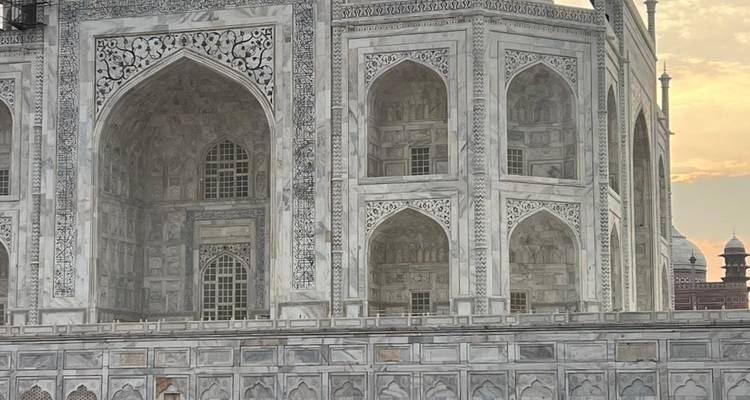 Detail of the marble façade of the Taj Mahal with intricate inlay work against a pastel evening sky.
