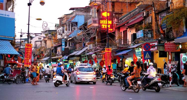 Drukke straatscène met scooters en neonreclames.