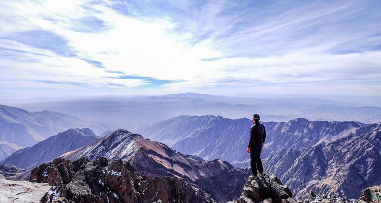 Hiker standing on a mountain peak overlooking vast ranges.