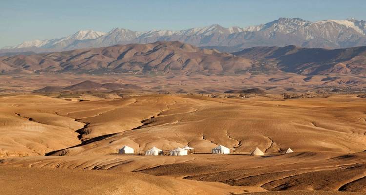 Desert landscape with tented camp and distant mountain range.