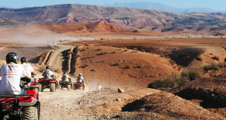 Gruppe fährt Quads auf Wüstenpisten mit Bergen im Hintergrund.