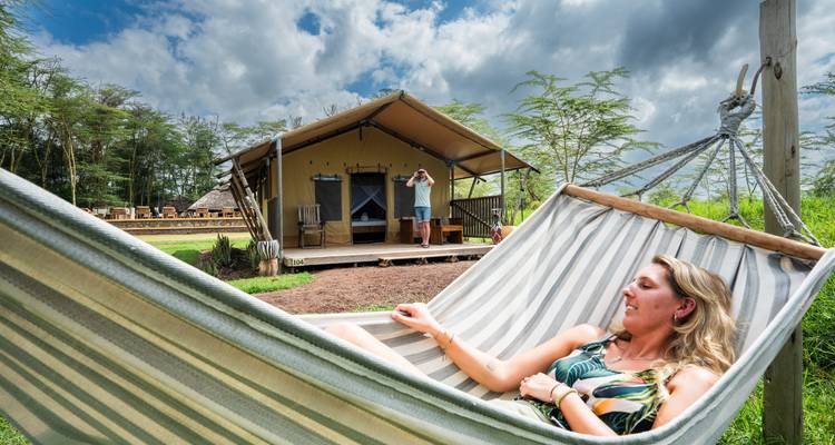 Frau entspannt in einer Hängematte mit Blick auf Zelte und Bäume.