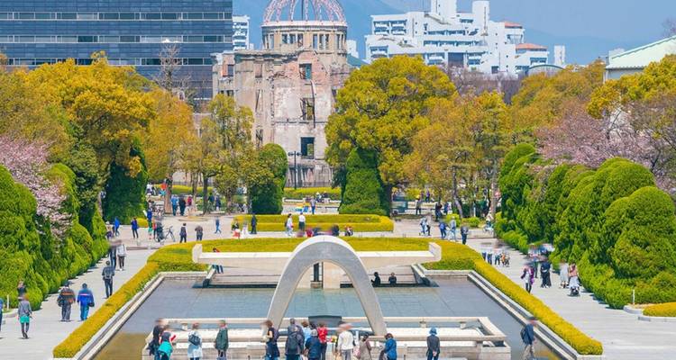 Menschen besuchen den Hiroshima-Friedensgedenkpark mit der Atombombenkuppel im Hintergrund.