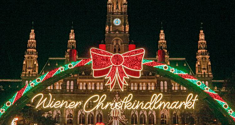 Festlicher beleuchteter Bogen empfängt Besucher nachts auf dem Christkindlmarkt in Wien.