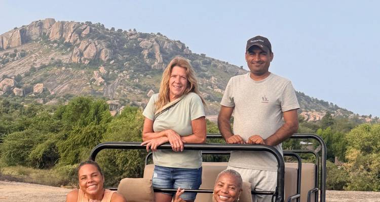Groep mensen in een safariwagen met rotsachtige heuvels op de achtergrond.