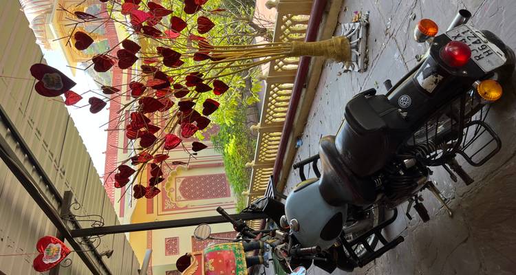 Motorfiets geparkeerd onder een schaduwrijke patio versierd met rode hartornamenten naast een kleurrijke, sierlijke gebouwgevel.