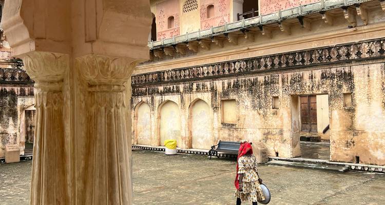 Binnenplaats van een oud fort met verweerde muren waar een vrouw in traditionele kleding metalen potten draagt.