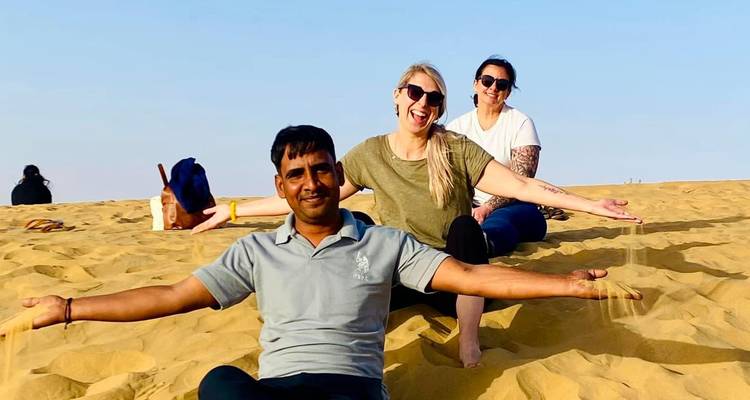 Lächelnde Reisende sitzen auf goldenem Wüstensand und lassen Körner durch ihre Hände rieseln