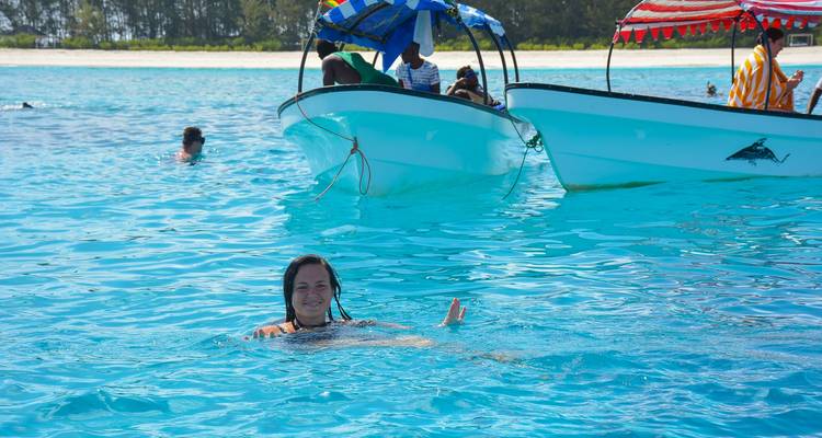 Tourists swimming in the ocean near boats, clear blue water.